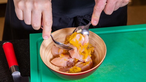 Hähnchenfleisch asiatisch zubereiten: In einer Schüssel wird die Geflügelbrust mit Curry und Salz mariniert.