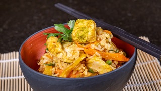 Reis mit Gemüse und Hähnchen asiatisch zubereitet als Gericht mit Stäbchen.