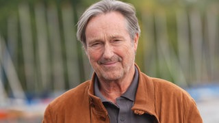 Helmut Zierl in brauner Lederjacke steht vor der Kamera und lächelt