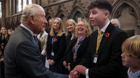 Ein älterer Herr mit weißen Haaren gibt einem jungen Mann im dunkelblauen Anzug und lockigem Haar die Hand. König Charles besucht die Kirche in Lichfield.