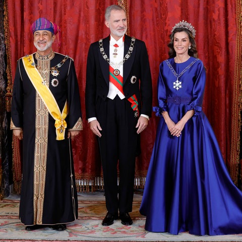 Königin Letizia trägt ein langes blaues Kleid und Juwelen. Ihr Mann, König Felipe, steht zwischen ihr und dem Sultan von Oman.