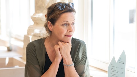 Jule Ronstedt im Interview: Die Schauspielerin stützt nachdenklich das Kinn auf die Hände und schaut aus dem Fenster.