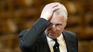 Der ehemalige Prinz Andrew fasst sich mit seiner Hand an den Kopf.