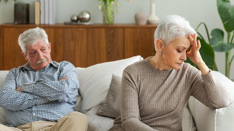 Ein Mann und eine Frau sitzen auf dem Sofa und sind genervt von ihren Macken.