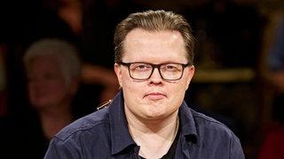 Angelo Kelly hat ein blaues Hemd an und schaut direkt in die Kamera