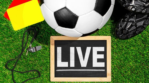Bildmontage von einem Fußball, einer gelben und einer roten Karte, einer Schiedsrichterpfeife und schwarzen Fußballschuhen hinter einer kleinen Tafel mit "LIVE" darauf.
