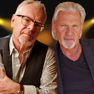 Nik Kershaw & Johnny Logan, montiert vor einem künstlichen Hintergrund, der an eine Bühne, beleuchtet von Scheinwerfern erinnert. 