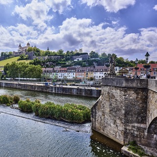 Man sieht rechts eine Fußgängerbrücke über einen Fluss, den Main, der in Richtung der Stadt Würzburg führt.