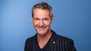 Der Sternekoch Christian Henze vor einem blauen Hintergrund.