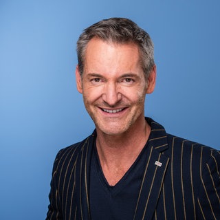Der Sternekoch Christian Henze vor einem blauen Hintergrund.
