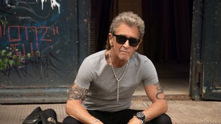 Peter Maffay sitzt auf einer Treppe, trägt eine Sonnenbrille und schaut in die Kamera