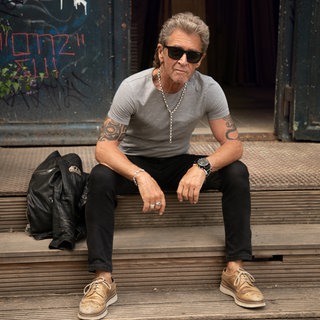 Peter Maffay sitzt auf einer Treppe, trägt eine Sonnenbrille und schaut in die Kamera