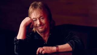 Chris Norman sitzt am Flügel und hat seinen Kopf in die Hand gestützt