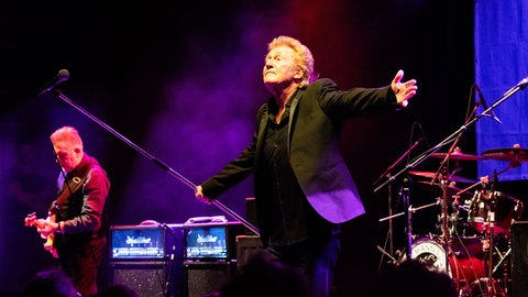 Musiker Robert Hard der Band Manfred Manns Earth Band steht auf der Bühne und streckt die Arme von sich
