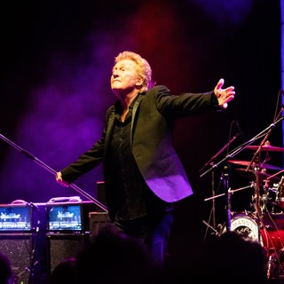 Musiker Robert Hard der Band Manfred Manns Earth Band steht auf der Bühne und streckt die Arme von sich