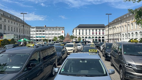 Etwa 70 Taxis stehen wegen einer Demo auf dem Karlsruher Marktplatz. Die Taxifahrer fordern strengere Regeln für Mietwagenunternehmen, die mit Uber, Wolt und Co. zusammenarbeiten. 