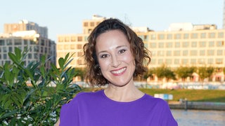 Bärbel Stolz steht vor einem Busch in einem lila Kleid