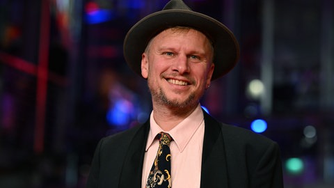 Robert Stadlober hat einen Hut auf und lacht in Richtung Kamera