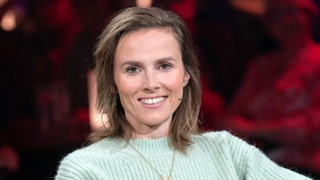 Die Schauspielerin Karin Hanczewski sitzt vor dem Publikum der MDR Sendung "Riverboat" und lächelt in die Kamera.