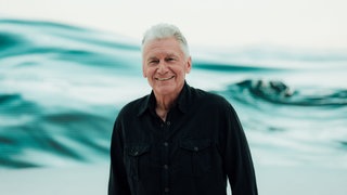 Rainhard Fendrich schaut in die Kamera und lacht.