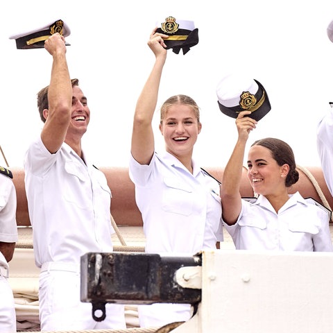 Prinzessin Leonor hebt ihre Matrosenmütze neben anderen Matrosen während einer Zeremonie lächelnd vom Kopf.