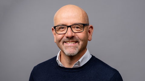 Porträt von SWR4 Moderator Jörg Assenheimer mit schwarzer Brille und blauem Pullover