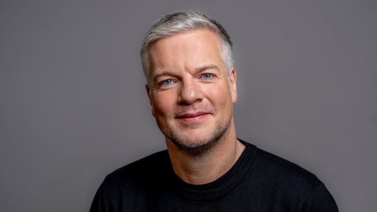 Porträt von Moderator Jens Vogt im schwarzen Pullover