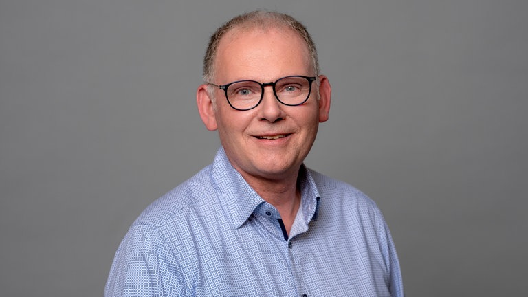 Porträt des lächelnden SWR4 Moderators Hans-Jürgen Finger in hellblau gemustertem Hemd