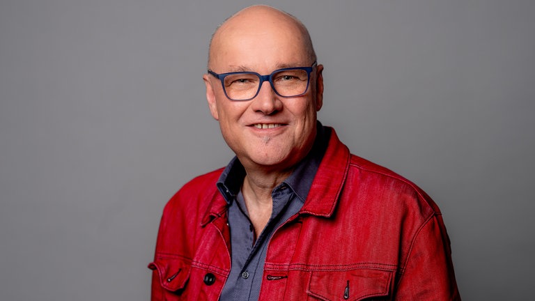 Porträt des SWR4 Moderators Johannes Riedel im blauen Hemd mit roter Jacke