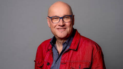 Porträt des SWR4 Moderators Johannes Riedel im blauen Hemd mit roter Jacke