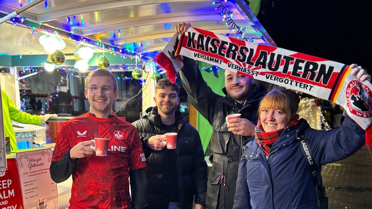Kaiserlautern-Fans halten ihren Schal hoch vor dem grünen SWR4 Adventsmobil auf dem Weihnachtsmarkt in Ramstein. 