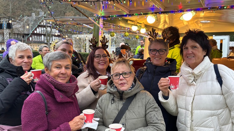 SWR4 Adventszauber: Eine Frauengruppe mit Rentiergeweihen auf dem Kopf trinken Glühwein und lächeln auf dem Weihnachnachtsmarkt in Bad Münster am Stein-Ebernburg in die Kamera.