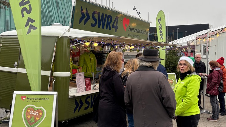 Weihnachtsmarkt in Fellbach: Das grüne SWR4 Adventsmobil steht bereit, davor unterhalten sich Besucher mit SWR4 Moderatorin Sabine Gronau.