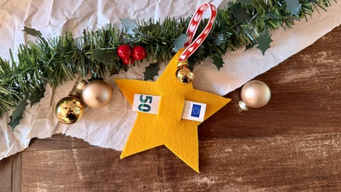 In der Mitte eines gelben Filzsterns ist durch zwei Schlitze ein eingerollter Geldschein gesteckt. Eine schöne Bastelidee, um an Weihnachten Geld zu verschenken.
