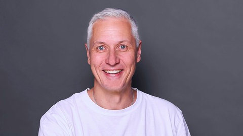 Porträt Stefan Frech vor grauer Wand mit hellem Shirt.