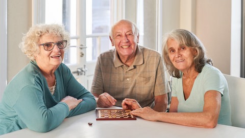 Senioren spielen ein Spiel am Tisch in ihrer WG, in der sie leben.