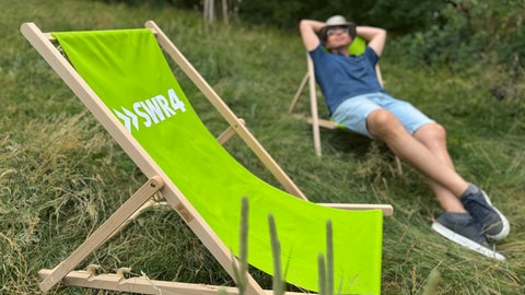 Sommerlich gekleideter Mann entspannt im Liegestuhl, im Vordergrund steht ein grüner Liegestuhl mit SWR4 Logo.