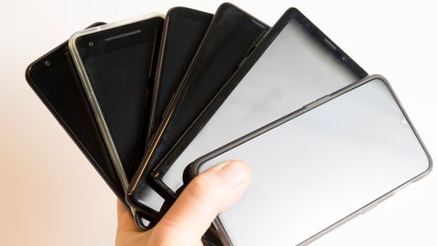 Alte Handys, die zuhause rumliegen in einer Hand, um dann Daten zu sichern, bevor das Smartphone entsorgt wird.
