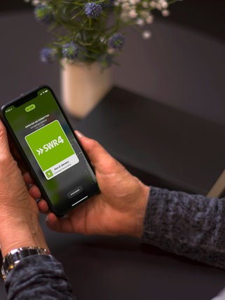 Eine Hand hält ein Smartphone, auf dem die SWR4 App geöffnet ist