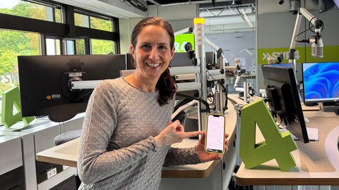 SWR4 Moderatorin Chrissie Weiß hält ein Handy mit dem SWR4 Whatsapp-Kanal in der Hand