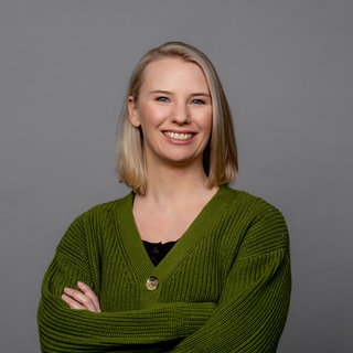 Julia Schönleber trägt eine grüne Strickjacke und lacht direkt in die Kamera