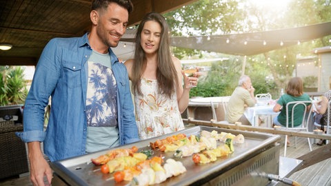 Ein Paar grillt auf einem Plancha-Grill Spieße.