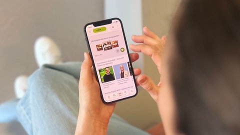 Die SWR4 App in ARD Sounds ist auf einem Smartphone zu sehen, auf dem eine Frau herumtippt.