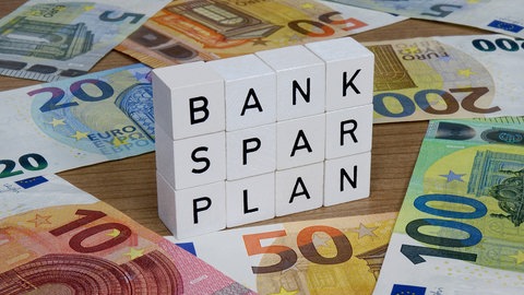 Auf Geldscheinen stehen Buchstabenwürfel mit dem Schriftzug Banksparplan