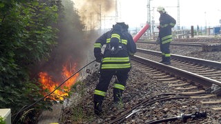 Feuerwehrleute kämpfen gegen einen Kabelbrand an einer Bahnstrecke