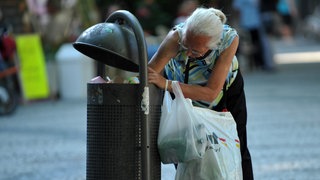 Ältere Frau durchsucht Mülleimer nach Pfandflaschen.