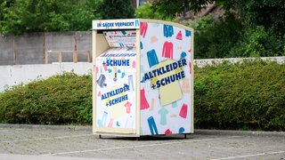 Ein Altkleidercontainer steht auf einem Supermarkt-Parkplatz.