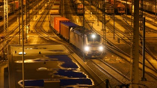 Güterzug fährt nachts in beleuchtetem Bahnhof.