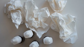 Verschiedene Nasensprays und benutzte Taschentücher auf einem Tisch.