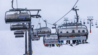 Wintersportler sitzen mit ihren Sportgeräten in den Sessellift-Gondeln der Feldbergbahn und lassen sich den Berg hinaufbringen